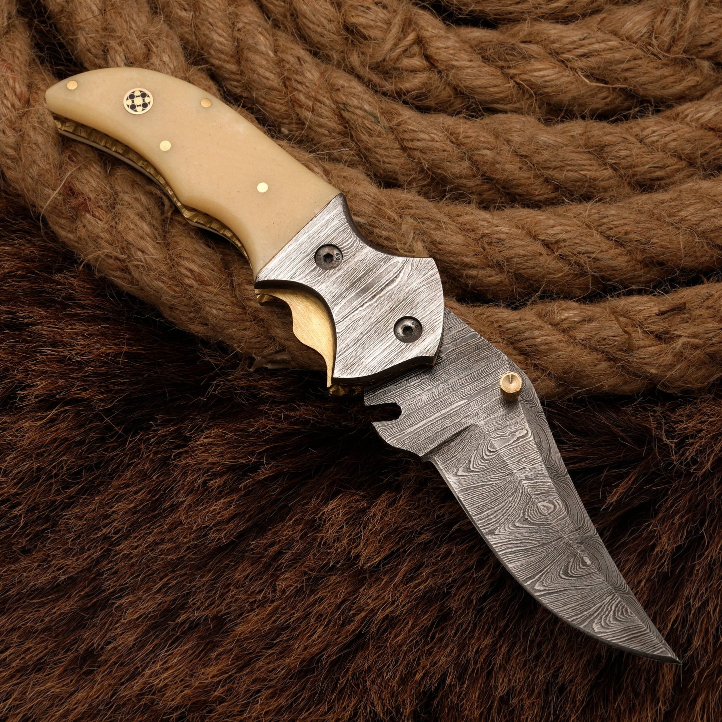 Damascus folding knife with a bone handle and a patterned steel blade, displayed against a rope and fur background for a rustic aesthetic.