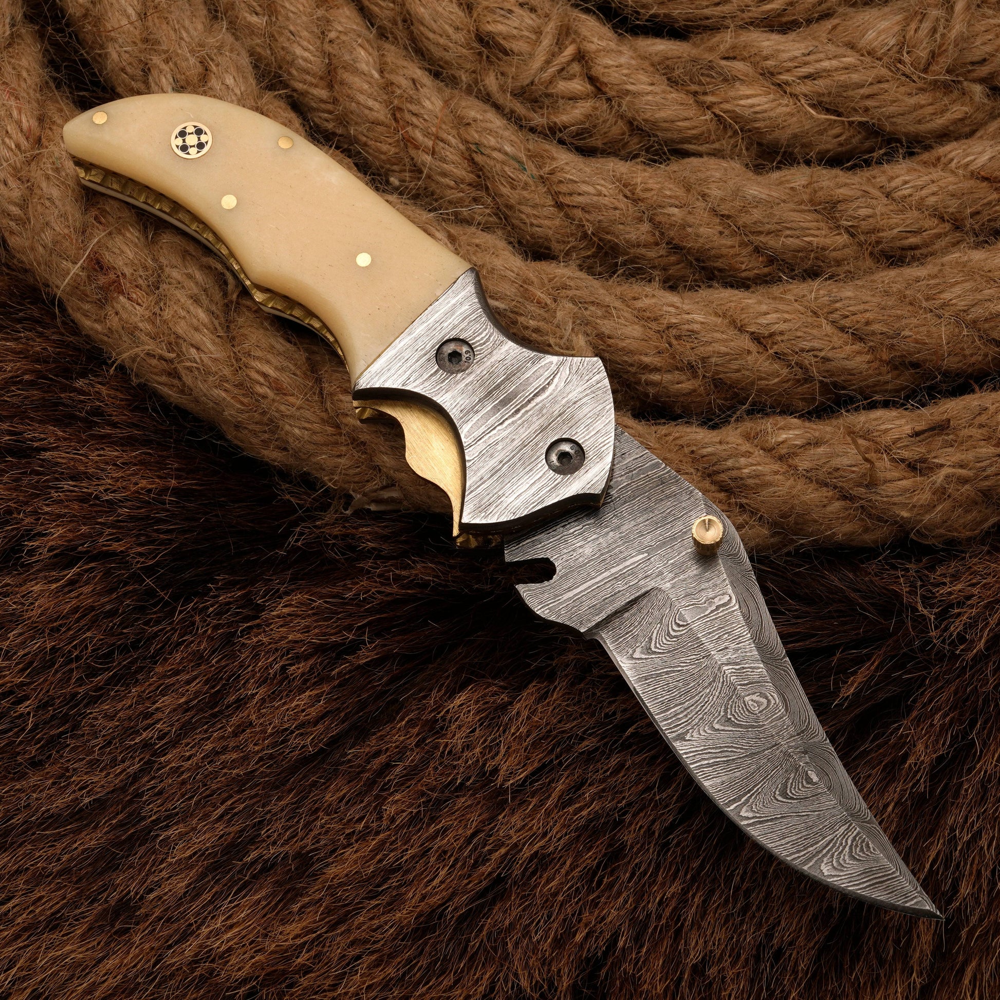 Damascus folding knife with a bone handle and a patterned steel blade, displayed against a rope and fur background for a rustic aesthetic.