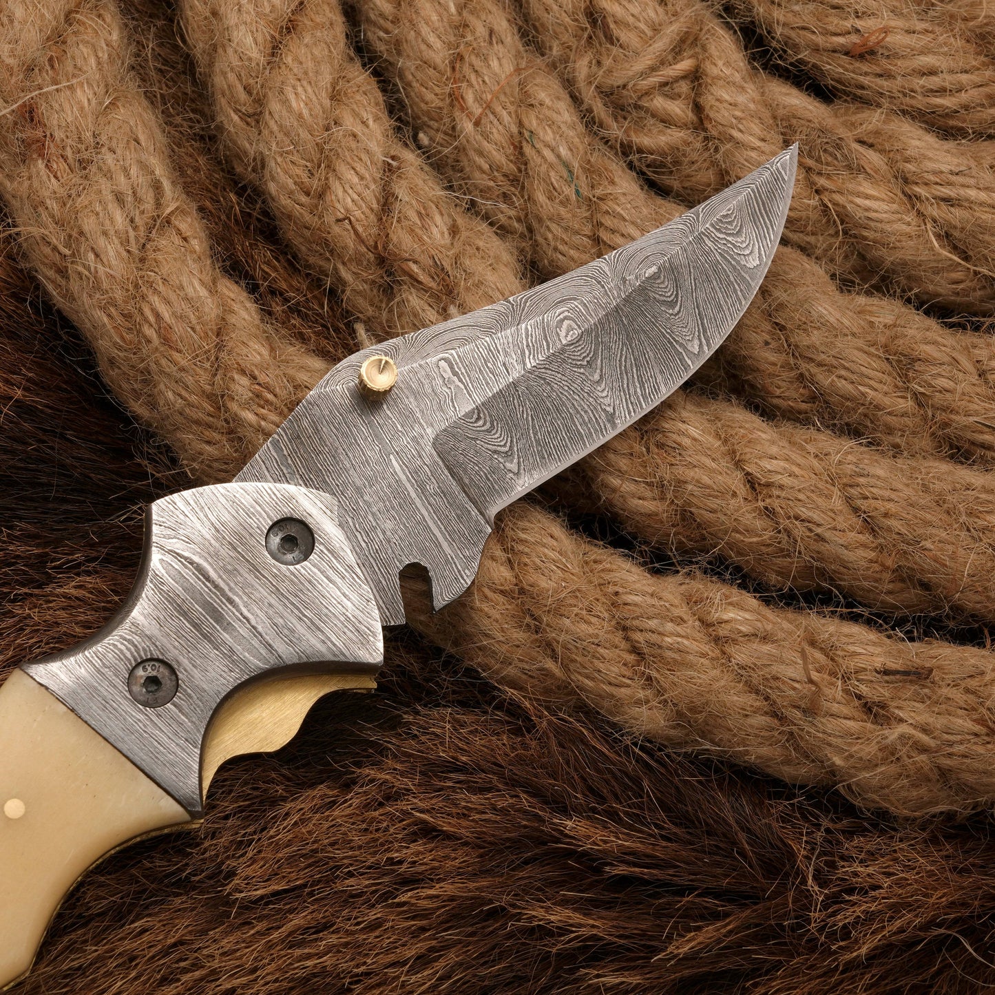 Close-up of the Damascus steel blade and bolster of a folding knife with a bone handle, emphasizing its detailed craftsmanship.
