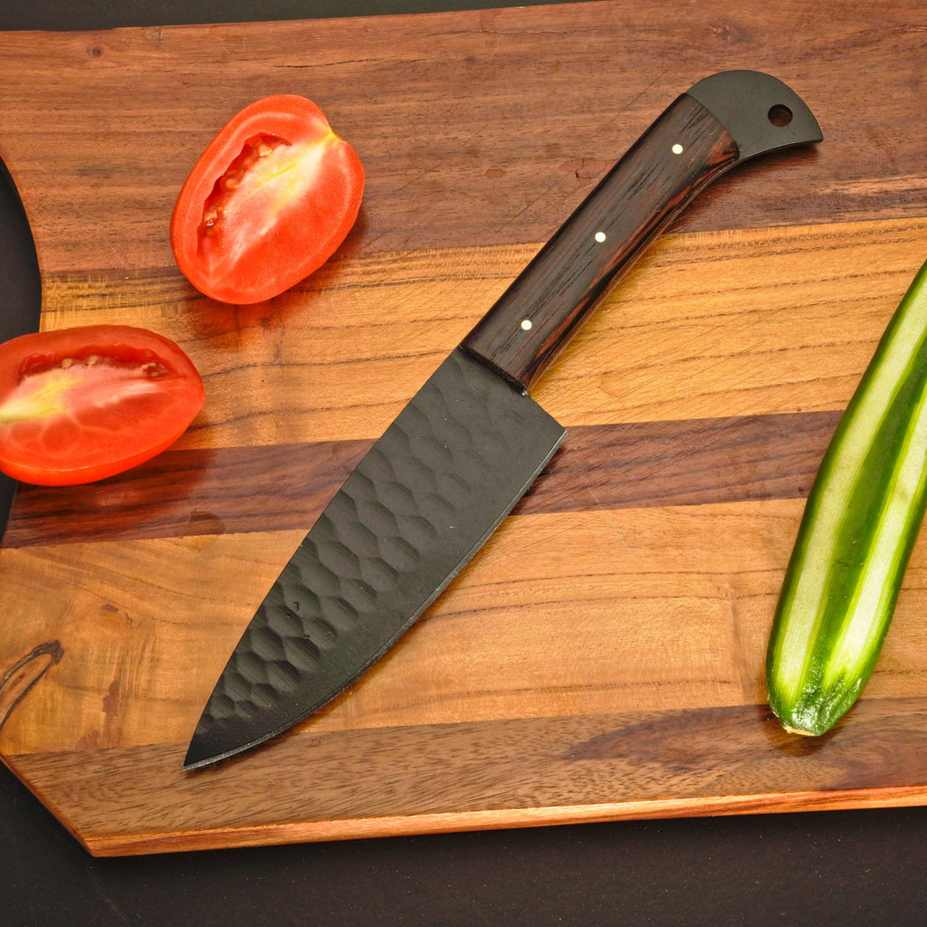 Knife with a wooden handle on a wooden cutting board with sliced tomatoes and a cucumber.